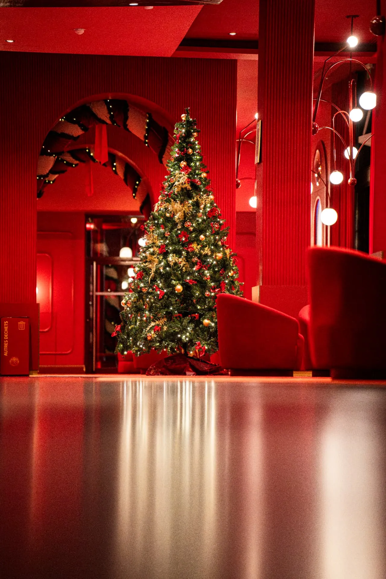 Sapin de Noël illuminé dans un espace rouge aux murs cannelés, reflet sur le sol brillant