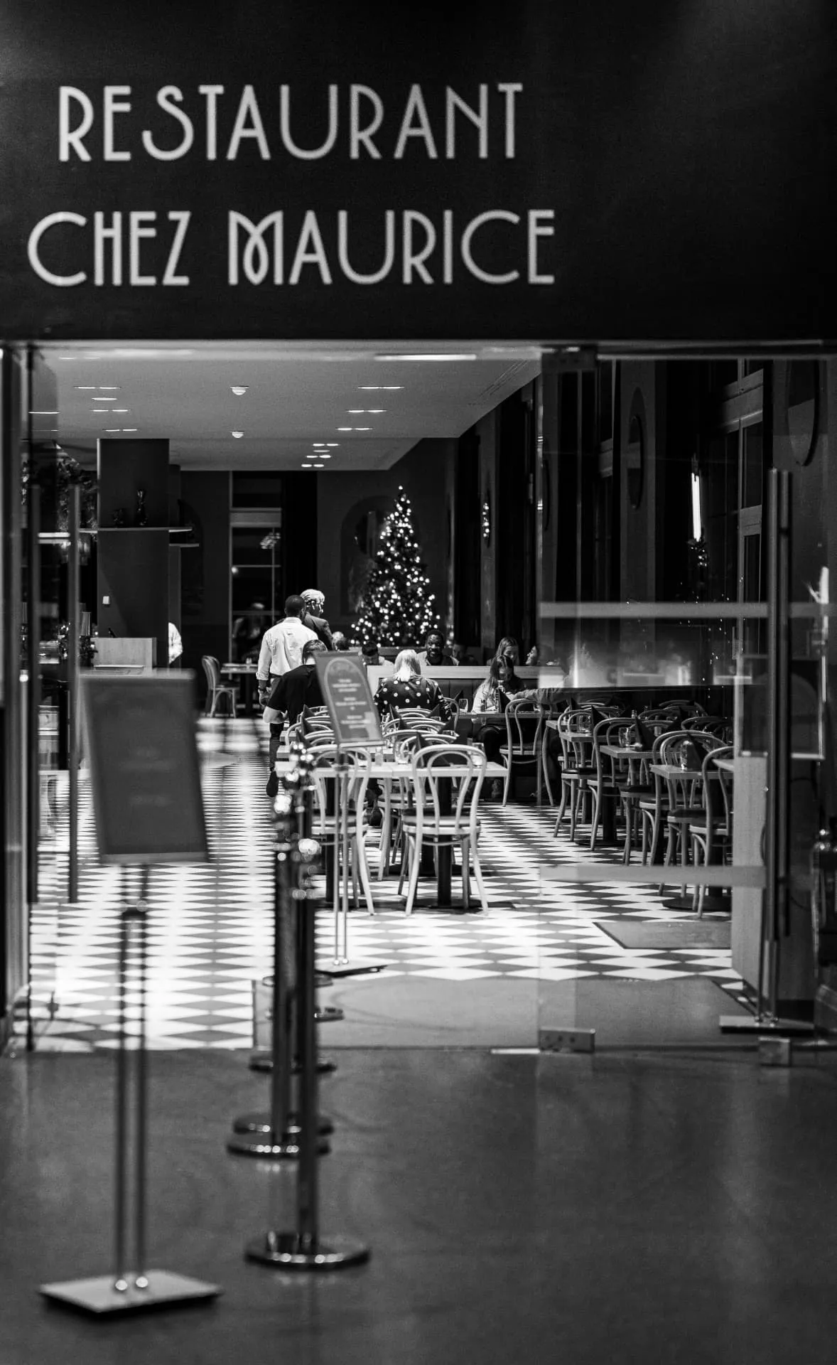 Entrée du restaurant Chez Maurice en noir et blanc, sol en damier et salle dressée