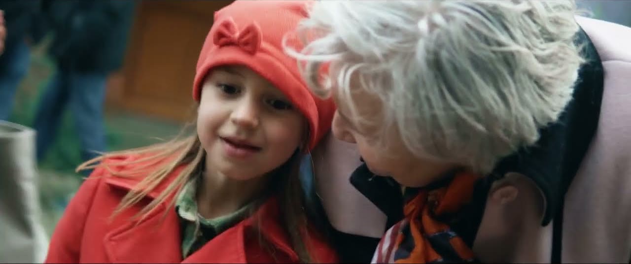 Une petite fille en bonnet rouge parle à l'oreille d'une femme aux cheveux blancs, photogramme du spot Pierre Morel