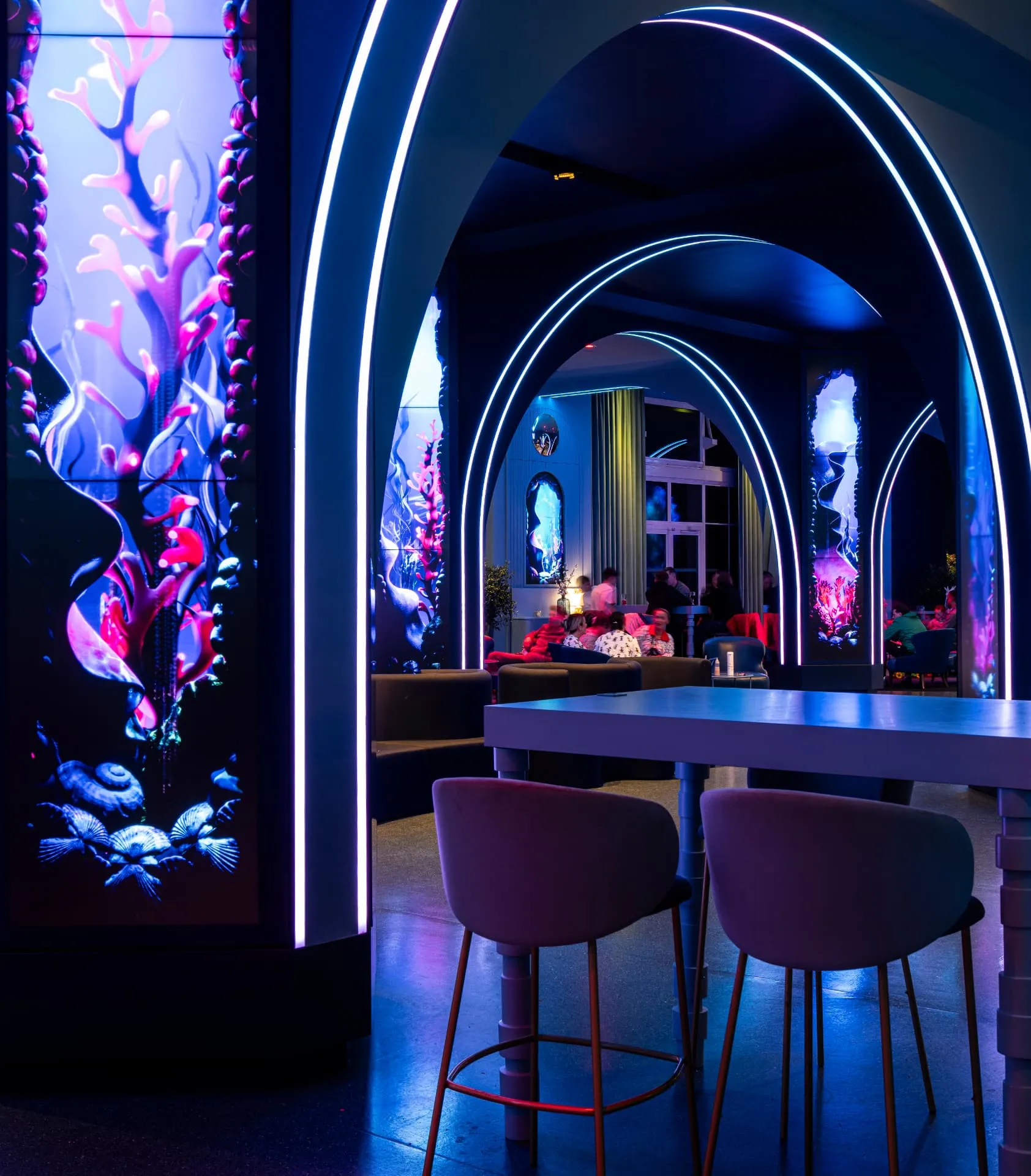 Tabourets devant une table haute, arches soulignées de lumière et écrans aux décors sous-marins