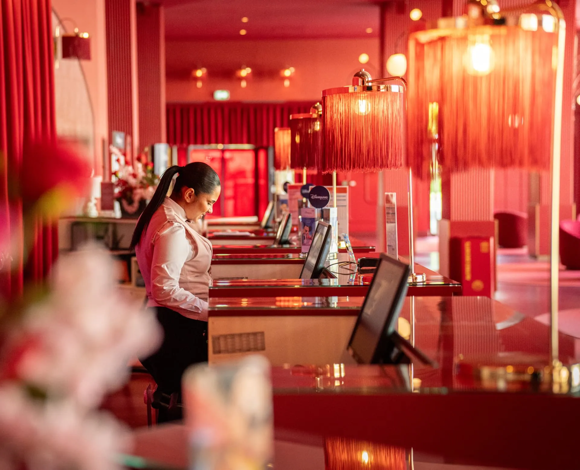 Comptoir d’accueil rouge et lampes à franges, une personne au travail derrière un écran