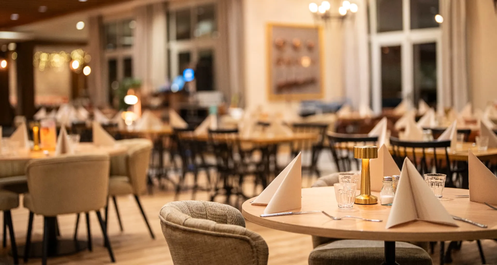 Salle de restaurant chaleureuse, tables rondes dressées de serviettes pliées et lampe dorée