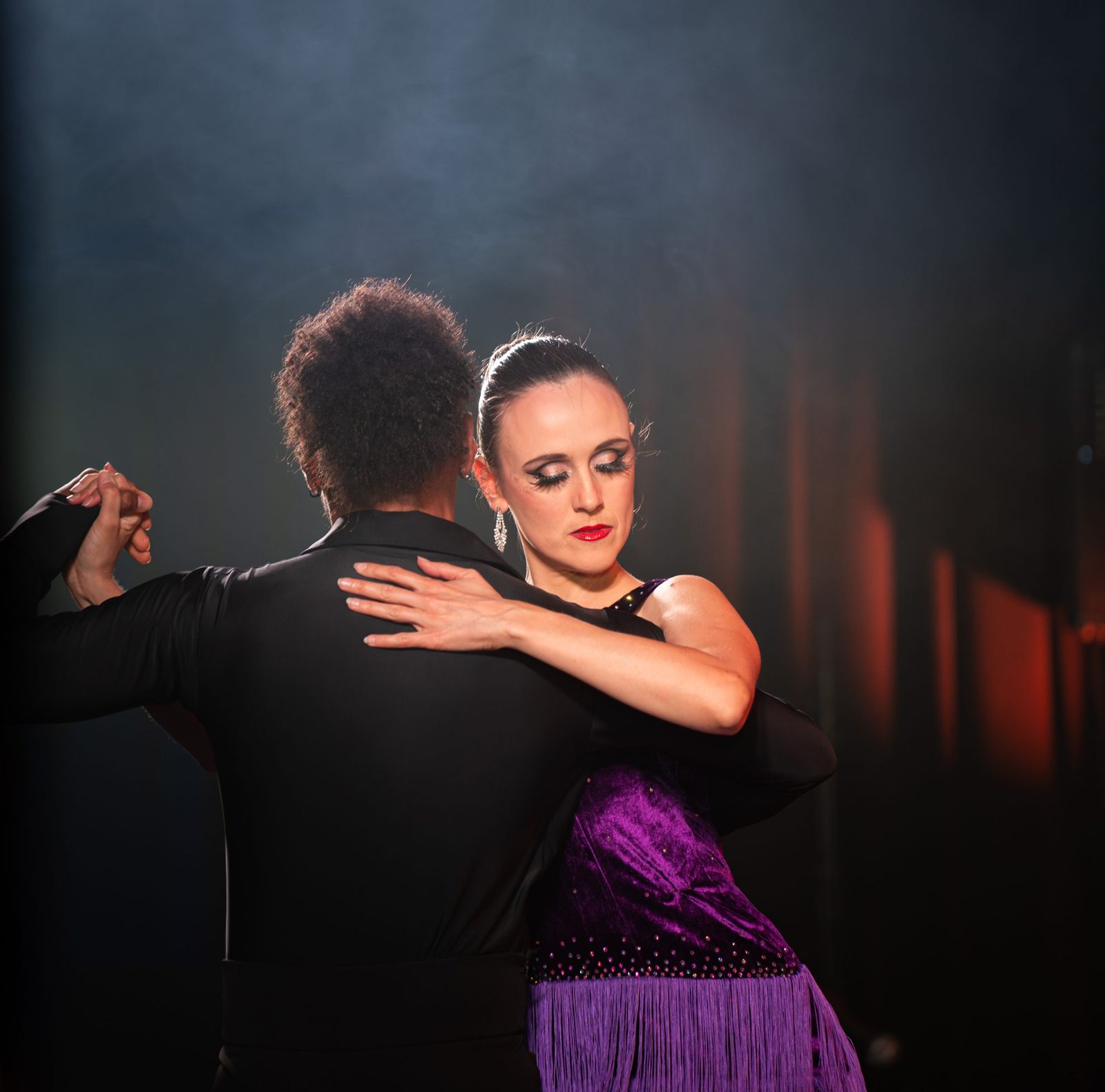 Couple de danseurs de flamenco saisi en mouvement sur scène, robe à franges et lumière rasante