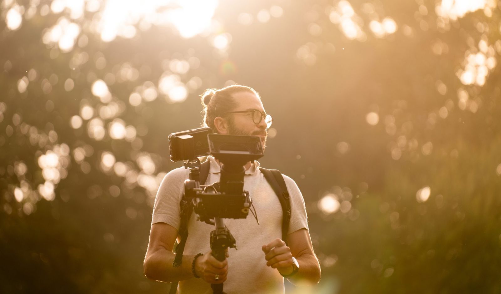 Cadreur en plein tournage en extérieur, caméra à l'épaule dans la lumière du soleil couchant